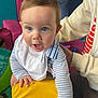 baby, child, blue_eyes, bib, striped_clothing, yellow_cushion, hand, adult, indoor, playroom, furniture, person, cute, curious, face, skin, hair, expression, support, colorful