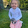 animal, casual_clothing, child, cute, daylight, flower, garden, grass, greenery, happy, kitten, kneeling, nature, outdoor, person, pet, pink_pants, smiling, white_shirt, young