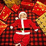 baby, celebration, child, christmas, cute, festive, gift_wrap, hat, holiday, holiday_decor, indoor, infant, plaid_blanket, presents, red_clothing, santa_costume, seasonal, small_feet, smiling, wrapped_gifts