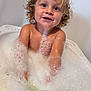 child, toddler, bath, foam, bubbles, curly_hair, happy, water, splashing, playful, skin, indoors, bathtub, smile, young, fun, cute, wet, joyful, person