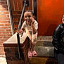 Evii is registered to the contest to win money with this photo: adult, brick_wall, child, concrete, hand_on_face, happy, leather_jacket, leggings, night, orange_door, outdoor, person, pink_slippers, playful, portrait, railing, sitting, smiling, urban, white_shirt