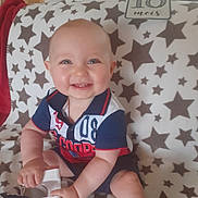 Lenny participe au concours pour gagner de l'argent avec cette photo : baby, blanket, cheerful, child, clothing, door, face, footwear, hand, happy, indoor, infant, polo_shirt, red_blanket, room, shorts, sitting, smiling, star_pattern, toy