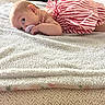 baby, infant, pacifier, striped_dress, towel, lying_down, couch, legs, soft_texture, indoor, child, person, cute, young, comfort, relaxing, fabric, home, cozy, blurred_background