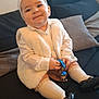 baby, toddler, child, white_headband, white_vest, white_socks, black_shoes, toy, keychain, couch, pillow, indoor, smiling, cute, happy, person, sitting, clothing, accessory, home