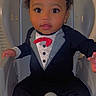 Jaxxon is registered to the contest to win money with this photo: baby, child, tuxedo, high_chair, cute, portrait, indoor, clothing, infant, smiling, face, person, sitting, cute_outfit, young_child, baby_boy, fashion, adorable, curly_hair, hands