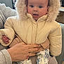 Logan joined the competition — help win amazing prizes! baby, child, infant, winter_jacket, hood, fur_trim, hand, adult_hand, sweater, patterned_pants, footwear, indoor, christmas_tree, decoration, face, expression, cute, warm_clothing, seated, cozy