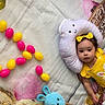 baby, child, yellow_outfit, bunny_design, plush_toy, cloud_pillow, colorful_eggs, easter_theme, festive, happy_easter_sign, blanket, headband, curly_hair, indoor, holiday, celebration, smiling_pillow, toy_bunny, basket, bright_colors