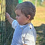 toddler, child, profile, side_view, overalls, striped_clothing, white_shirt, curly_hair, fence, outdoor, daylight, nature, grass, hand, portrait, young_child, casual_clothing, baby, looking, sunlight
