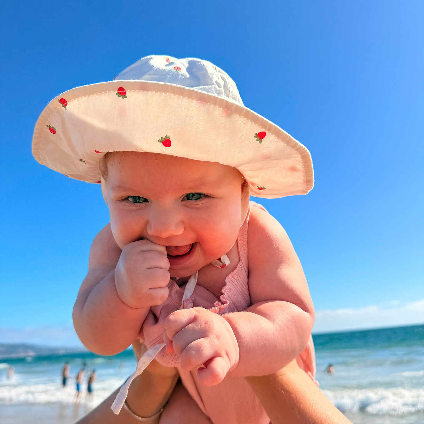 Sophia joined the competition — help win amazing prizes! baby, child, sun_hat, strawberry_print, beach, ocean, sky, smile, hand, arm, water, waves, summer, sunny, outdoor, cute, playful, person, happy, infant