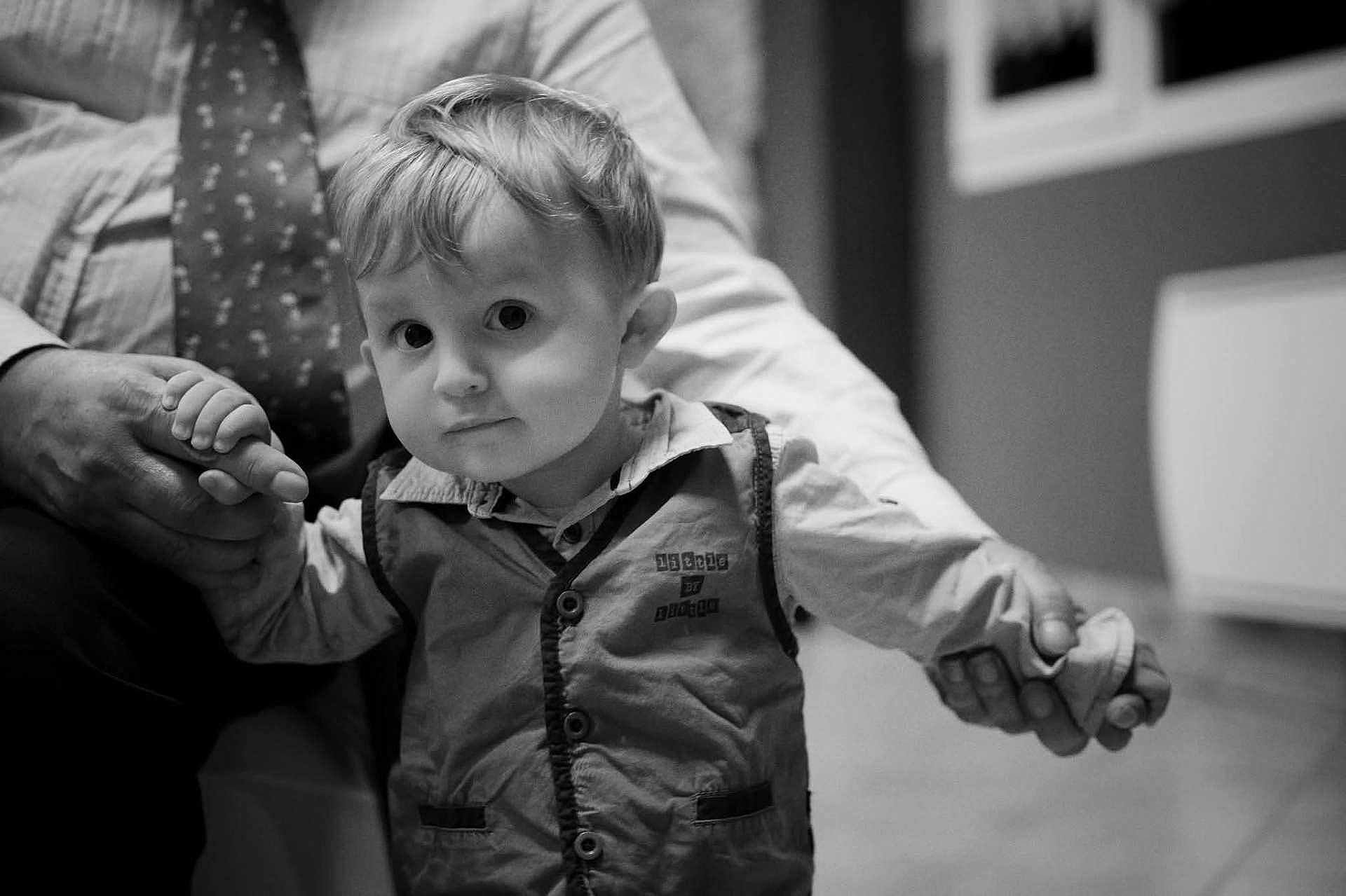 Lucas participe au concours pour gagner de l'argent avec cette photo : toddler, child, person, hand, adult, holding_hands, clothing, vest, shirt, face, hair, indoors, floor, window, tie, black_and_white, portrait, expression, curious, closeup