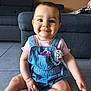 Salomé participe au concours pour gagner de l'argent avec cette photo : baby, child, smiling, indoor, denim_overalls, pink_shirt, pacifier, floor, tile_floor, sofa, pillow, cute, happy, portrait, sitting, infant, home, person, young_child, casual_clothing