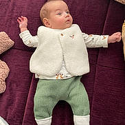 Hélène Vaishnavi participe au concours pour gagner de l'argent avec cette photo : baby, infant, newborn, lying_down, white_fleece_vest, long_sleeve_shirt, green_knit_pants, patterned_socks, maroon_couch, pillow, blanket, hand, face, wide_eyes, soft_texture, indoor, cozy, portrait, cute, expression