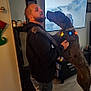 man, dog, hug, indoor, living_room, television, video_game, holiday_lights, festive, casual_clothing, black_hoodie, jeans, large_dog, spotted_dog, flooring, decorations, cabinet, shelf, joy, affection