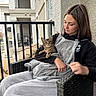 Delilah is registered to the contest to win money with this photo: apartment, balcony, blanket, casual_wear, cat, chair, comfort, daylight, fur, gray_clothing, looking_down, outdoor, person, pet, railing, relaxing, seated, tabby_cat, wicker_furniture, window