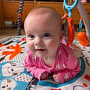Sophia is registered to the contest to win money with this photo: baby, infant, pink_clothing, play_mat, toy, animal_design, blue, orange, cute, happy, face, child, indoor, wooden_furniture, smiling, colorful, toddler, crawling, playtime, closeup