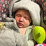 baby, sleeping, blanket, car_seat, plush_toy, toy, child, infant, face, closed_eyes, cozy, floral_pattern, fabric, comfort, soft_texture, cute, peaceful, indoors, resting, bundle