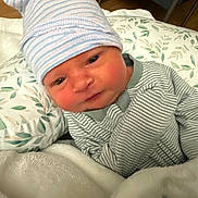 Mason joined the competition — help win amazing prizes! baby, infant, hat, striped_clothing, blanket, pillow, face, person, newborn, cozy, indoor, cute, sleepwear, headwear, soft_fabric, resting, portrait, young_child, expression, comfort