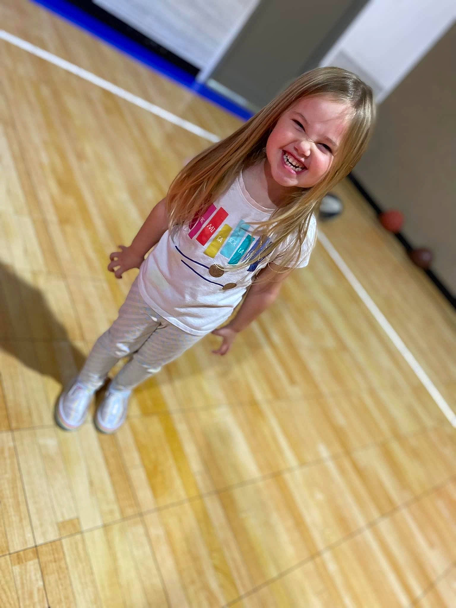 Adalyn is registered to the contest to win money with this photo: face, floor, flooring, happy, hardwood, human_leg, joy, knee, laminate_flooring, leisure, long_hair, person, sitting, smile, sportswear, t_shirt, thigh, toddler, varnish, wood