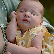 Verena is registered to the contest to win money with this photo: baby, sleeping, child, infant, yellow_dress, daisy_pattern, arm, hand, soft_focus, outdoor, portrait, peaceful, skin, face, person, holding, close_up, expression, nature, relaxation