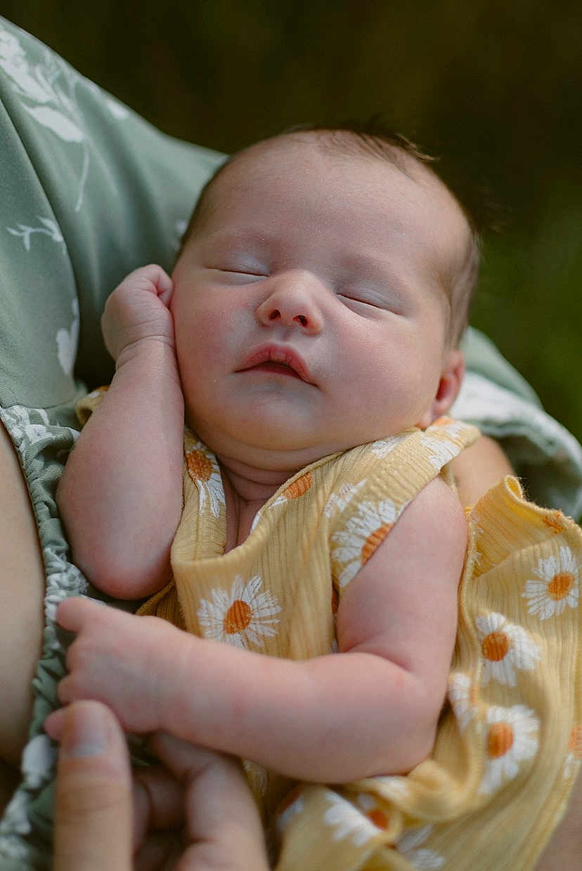 Verena is registered to the contest to win money with this photo: baby, sleeping, child, infant, yellow_dress, daisy_pattern, arm, hand, soft_focus, outdoor, portrait, peaceful, skin, face, person, holding, close_up, expression, nature, relaxation