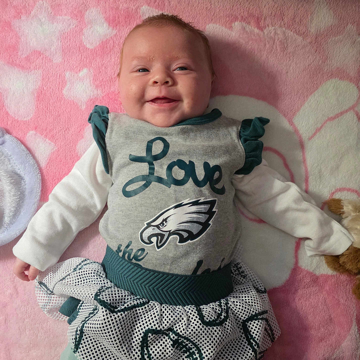 Hannah joined the competition — help win amazing prizes! apparel, baby, blanket, child, clothing, cute, face, happy, indoor, infant, long_sleeve, lying_down, pattern, person, pink, smiling, soft, stuffed_animal, toy, tutu