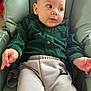Kenzo a rejoint le concours — aidez-le/la à gagner de superbes lots ! baby, child, infant, green_shirt, beige_pants, chair, seat, looking_away, curious, indoor, padded_chair, person, young_child, casual_clothing, hands, face, head, expression, relaxed, comfortable