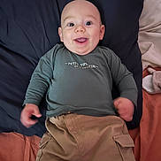 Kenzo participe au concours pour gagner de l'argent avec cette photo : baby, child, smiling, face, clothing, long_sleeve, pants, bed, pillow, blanket, happy, person, infant, lying_down, cute, indoors, young_child, casual_wear, tongue_out, relaxed