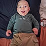 baby, child, smiling, face, clothing, long_sleeve, pants, bed, pillow, blanket, happy, person, infant, lying_down, cute, indoors, young_child, casual_wear, tongue_out, relaxed