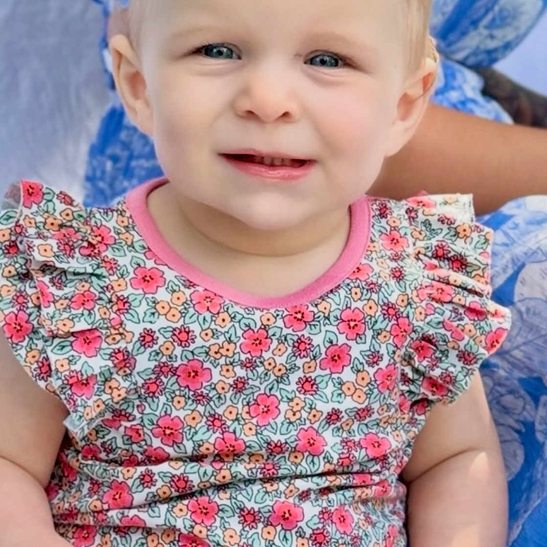 Veralyn is registered to the contest to win money with this photo: baby, blond_hair, blue_eyes, casual, child, closeup, cute, face, floral_outfit, hands, happy, indoor, infant, person, portrait, sitting, skin, smiling, soft_light, young_child