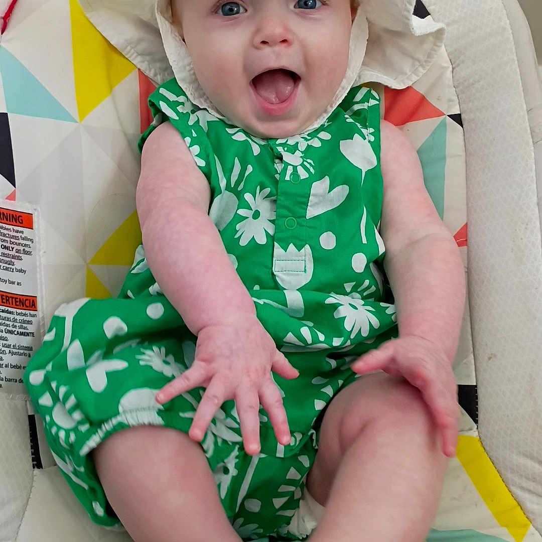 Indi joined the competition — help win amazing prizes! baby, child, infant, hat, white_hat, green_clothing, floral_pattern, baby_seat, colorful, happy, smiling, arms, legs, indoor, cute, playful, person, face, mouth_open, blue_eyes
