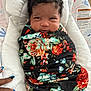 baby, infant, blanket, floral_pattern, swaddled, cushion, baby_seat, face, curly_hair, hand, nail_polish, pattern, comfort, indoor, portrait, child, smile, person, warning_label, fabric