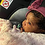 baby, infant, blanket, pink, hat, pacifier, car_seat, warning_label, curly_hair, side_profile, close_up, soft_texture, child, cute, bundle, looking, warm, indoor, portrait, adorable