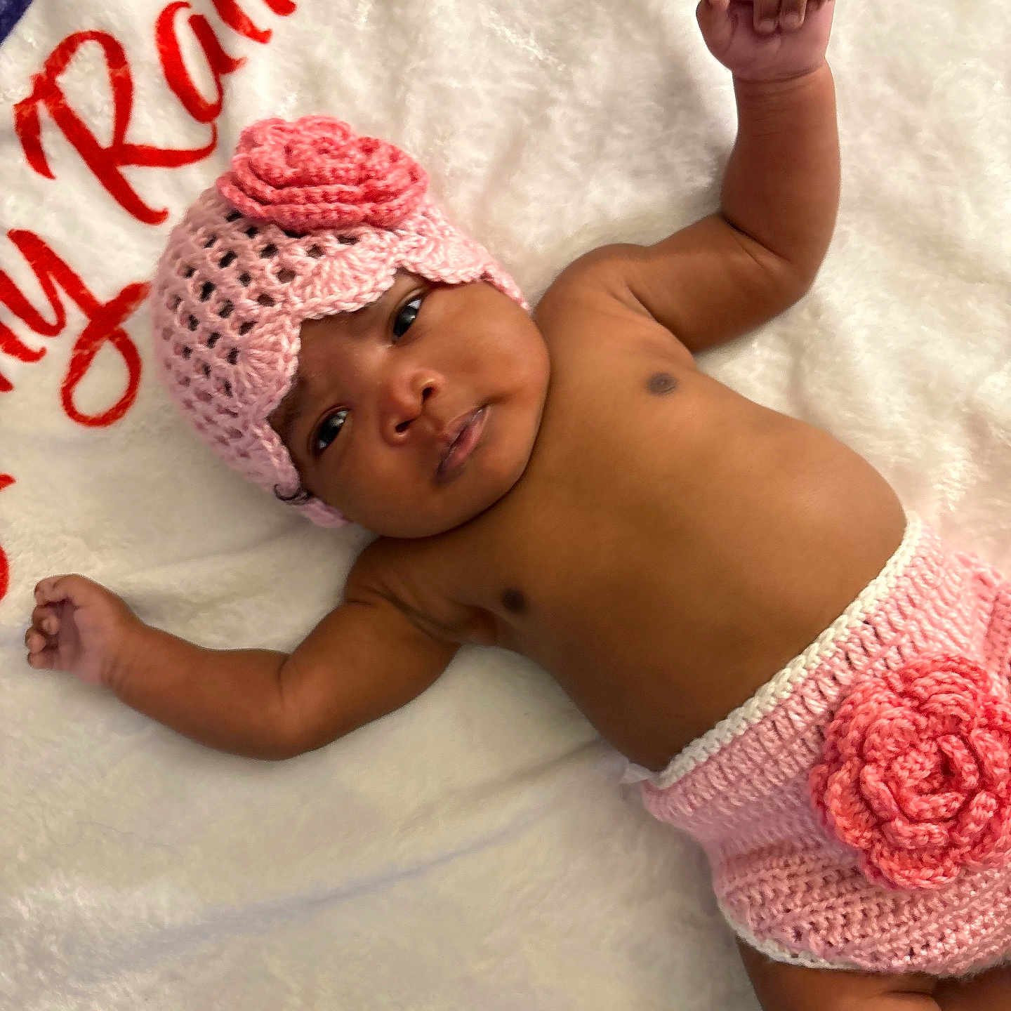 Essence joined the competition — help win amazing prizes! arms_up, baby, blanket, calm, child, closeup, comfort, crochet_hat, crochet_shorts, curious, cute, flower, headwear, indoors, infant, lying_down, pink, portrait, skin, soft_texture