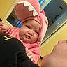 baby, child, costume, pink, dinosaur, hood, face, indoor, person, holding, adult, expression, sleepy, unimpressed, home, window, yellow_wall, clothing, cute, portrait