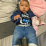 baby, denim_jacket, jeans, hat, blue_bow, blanket, stuffed_animal, pillow, bed, clothing, infant, child, cute, portrait, indoor, person, face, expression, sitting, soft_toy