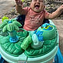 baby, child, smiling, joyful, walker, toy, outdoor, concrete, tree_roots, car, green, pink_shirt, person, happy, infant, playful, sunshine, reaching, sitting, cute