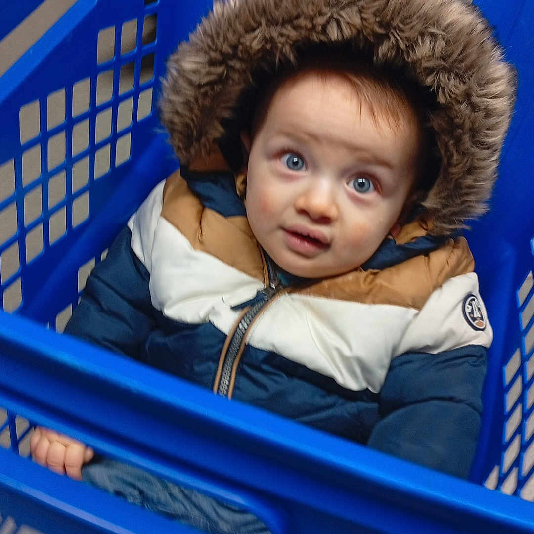 Gaby participe au concours pour gagner de l'argent avec cette photo : baby, basket, bonnet, cap, clothing, coat, crib, face, furniture, hat, head, hood, infantbed, jacket, laundry, person, photography, portrait, shoppingbasket, shoppingcart