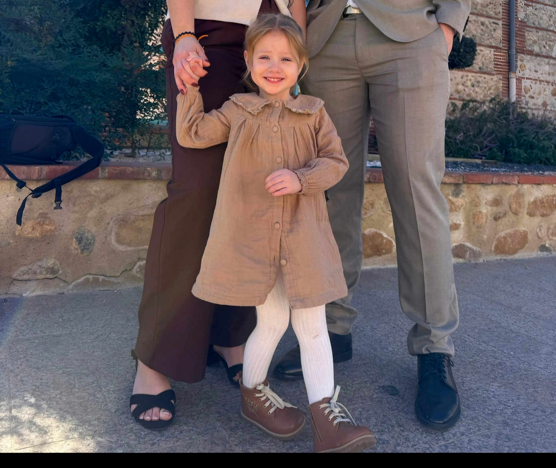 Luna a rejoint le concours — aidez-le/la à gagner de superbes lots ! child, toddler, girl, smile, holding_hands, dress, tights, boots, shoes, parents, adult_legs, sandals, suit_pants, stone_wall, pavement, backpack, greenery, outdoor, portrait, happy