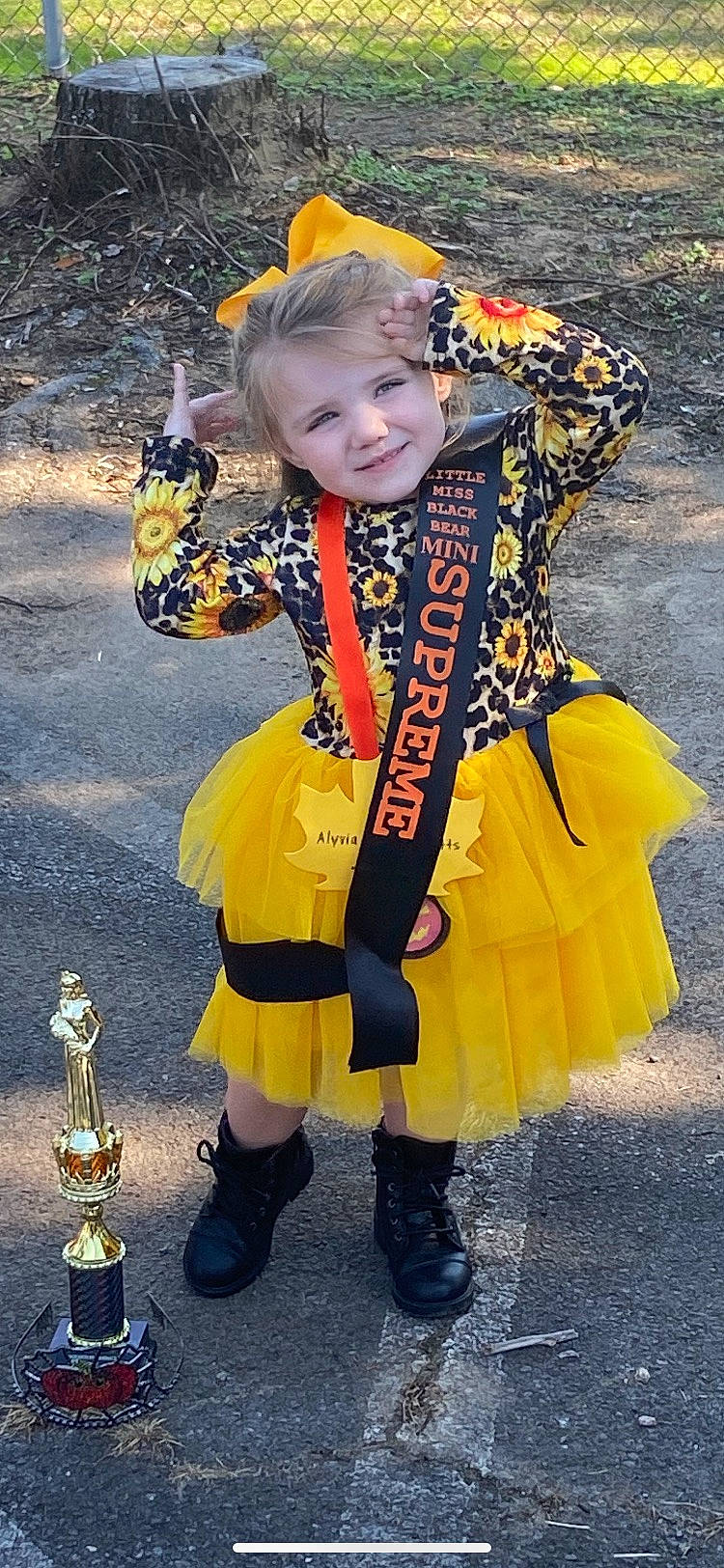 Alyvia is registered to the contest to win money with this photo: asphalt, boot, child, costume, costume_hat, dress, event, face, fun, happy, hat, headgear, joy, orange, pattern, person, sleeve, smile, street_fashion, toddler