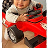 baby, child, smiling, toy_car, red, indoors, floor, steering_wheel, checkered_pattern, racing, seat, cute, happy, person, clothing, play, young_child, head, face, hand