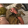 cat, tabby_cat, furry, pet, sleeping, lying_down, relaxed, indoor, bed, bedroom, pillow, blanket, person, lap, arm, remote_control, cozy, cuddling, photograph, smartphone_screenshot