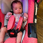 Nova Rios is registered to the contest to win money with this photo: baby, infant, car_seat, child, straps, pink, seat, clothing, pacifier, wood_floor, safety_belt, cute, indoors, person, newborn, face, legs, head_support, bright_colors, expression