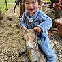 child, toddler, smiling, blue_outfit, stone_statue, deer_statue, outdoor, garden, gravel, plants, pottery, happy, playful, nature, rustic, toy, person, cute, young_child, daylight