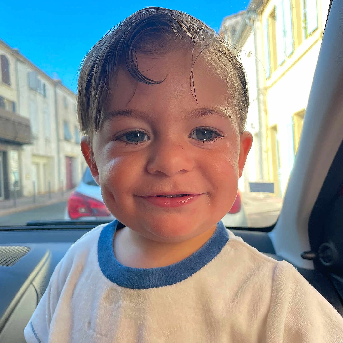 Kellyam a rejoint le concours — aidez-le/la à gagner de superbes lots ! blue_eyes, buildings, car_interior, casual_clothing, child, cute, daylight, dimples, face, happy, portrait, smile, street, sunny, toddler, vehicle, wet_hair, white_shirt, window, young_child