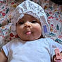 baby, child, face, tongue, white_clothing, headwear, blanket, floral_pattern, playful, cheeks, lying_down, cute, infant, indoors, pacifier_clip, pink, expression, person, closeup, soft_lighting