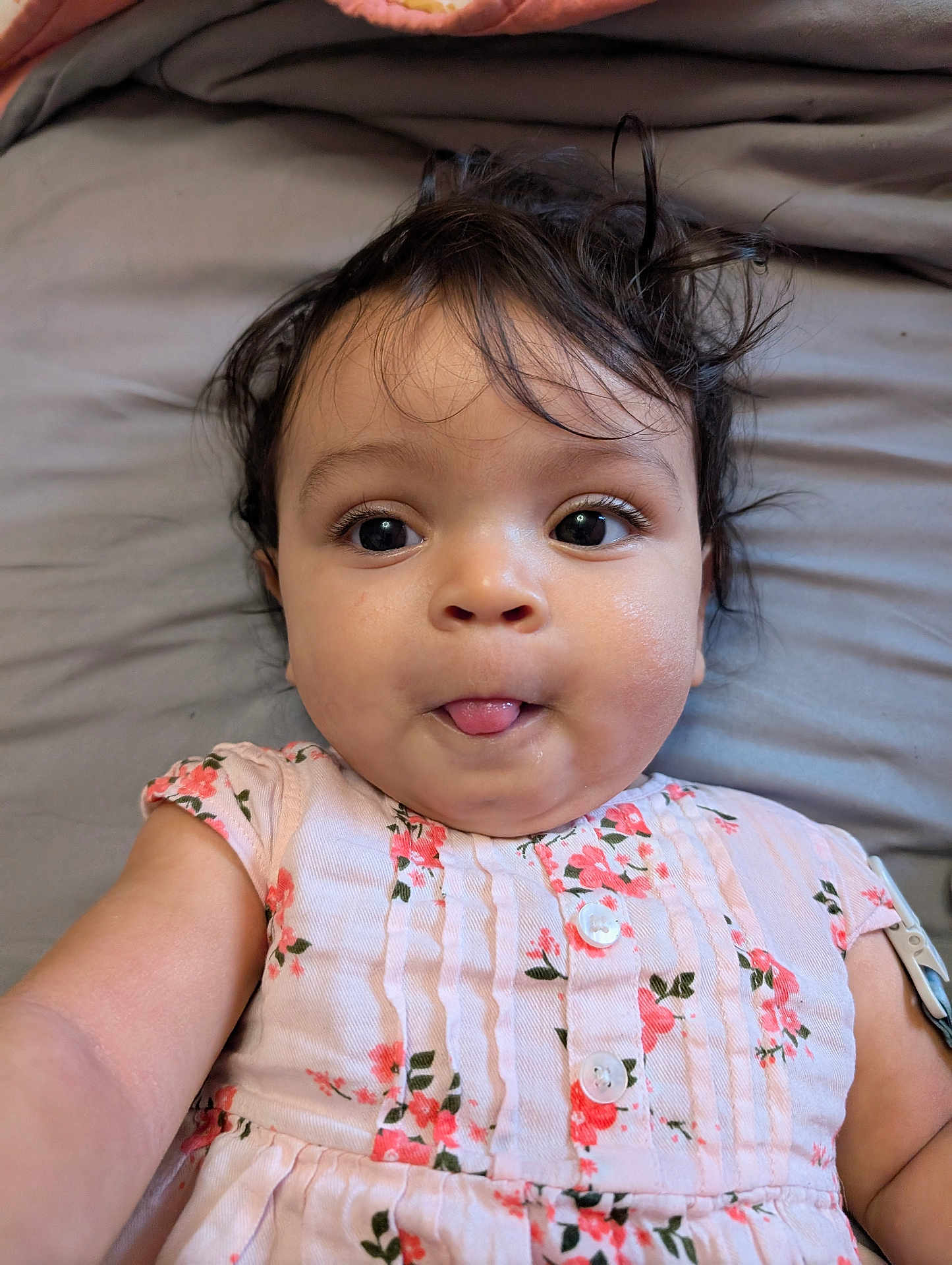 Naomi joined the competition — help win amazing prizes! baby, child, face, tongue, hair, floral_dress, pink, skin, eyes, infant, cute, portrait, lying_down, expression, person, indoor, soft_surface, closeup, adorable, playful