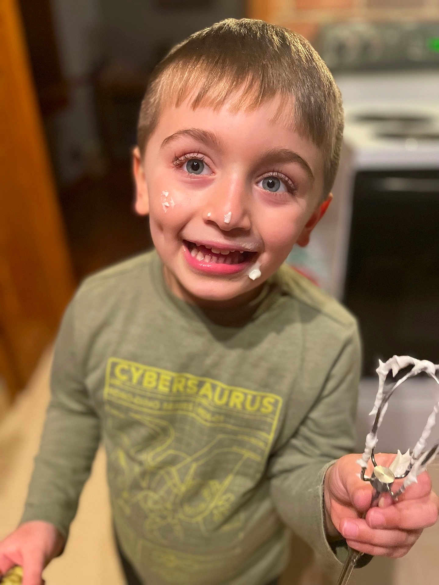 Mason is registered to the contest to win money with this photo: child, boy, smiling, whipped_cream, face_cream, kitchen, mixer_beater, green_shirt, messy_face, happy, indoor, cooking, baking, playful, young, person, portrait, short_hair, light, home