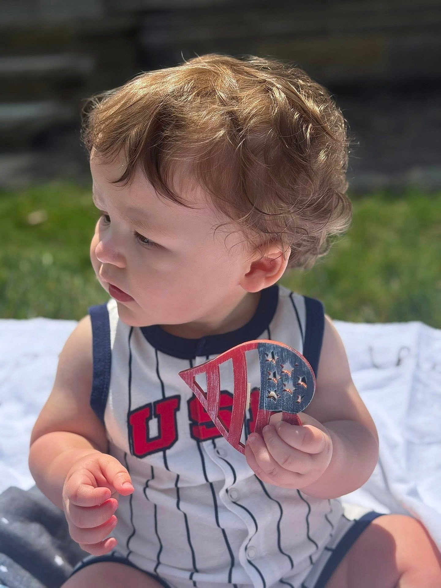 Matthew is registered to the contest to win money with this photo: toddler, child, curly_hair, outdoor, sunlight, grass, toy, holding, usa, clothing, sitting, baby, portrait, summer, cute, young_child, play, casual, daytime, skin