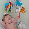 baby, blanket, child, colorful_toy, curious, cushion, diaper, expression, face, hand, head, indoor, infant, person, play, reaching, soft_light, toy, wall, young_child