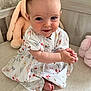 baby, child, smiling, dress, clapping, plush_toy, bed, cute, happy, indoor, person, toddler, patterned_clothing, foot, hand, face, head, furniture, soft_toy, infant
